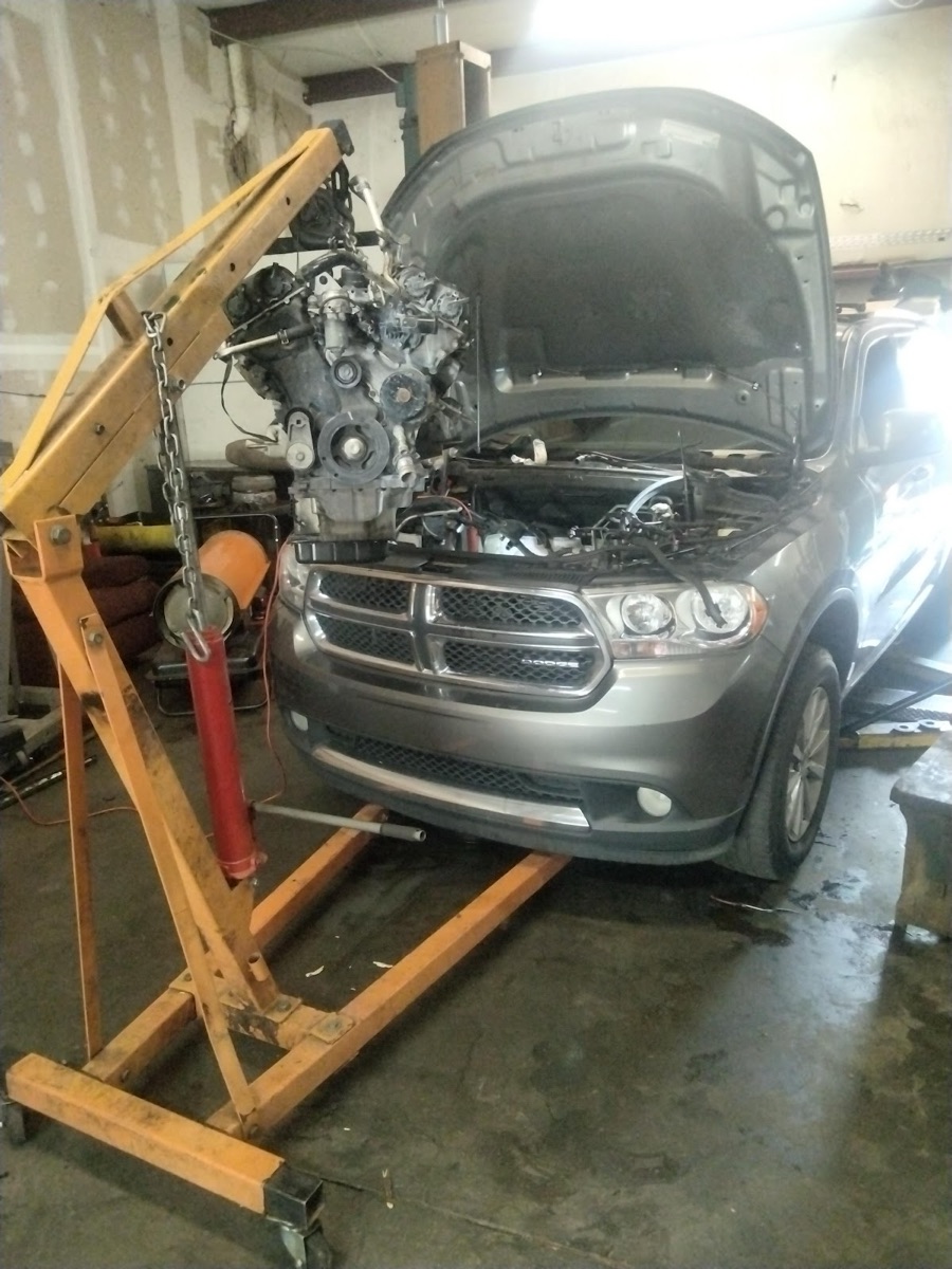 An engine pulled on a hoist next to an SUV in the service bay